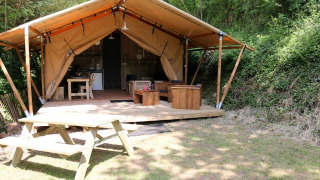 Tenda safari Safari Lodge XL con mobili in legno su veranda e tavolo da picnic in ambiente boschivo