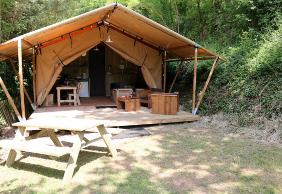 Safari Lodge XL safari tent with wooden furniture on deck and picnic table in a lush forest setting