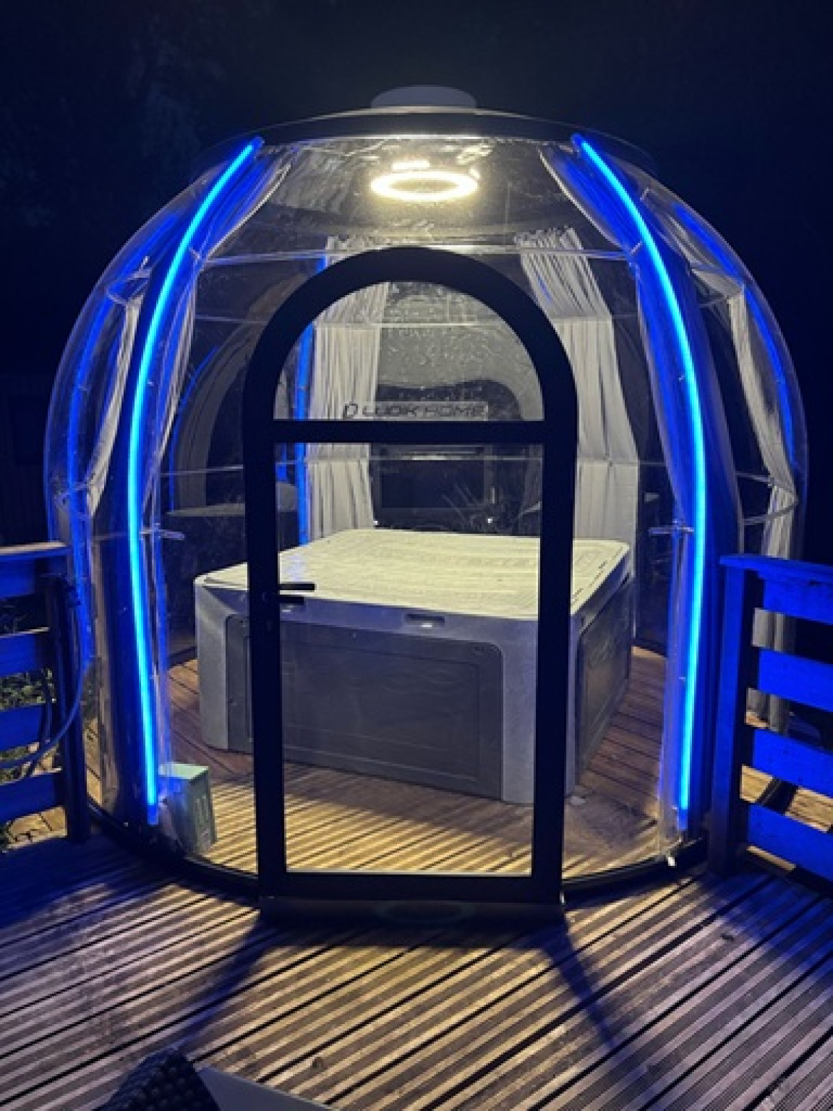 Verlichte transparante koepel met jacuzzi binnenin, op een houten terras bij Flower Camping de la Trye.