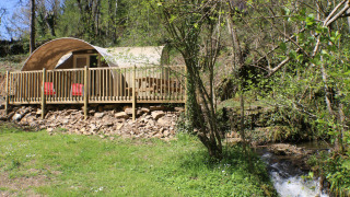 Tienda safari CocoSweet con terraza de madera y sillas rojas, junto a un arroyo en el bosque.
