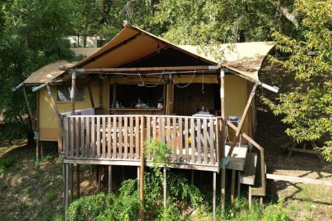 Tenda safari Luxury Lodge Diva con terrazza in legno, circondata dal verde e alberi sotto il sole.
