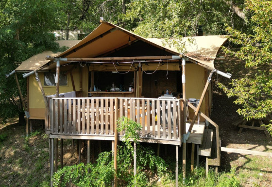 Tienda de safari Luxury Lodge Diva con terraza de madera, rodeada de vegetación y árboles al sol.