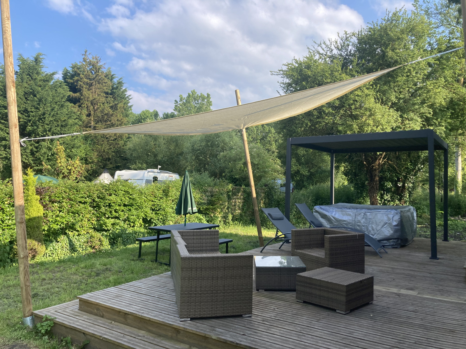 Buitenterras met rotanmeubels, schaduwdoek en jacuzzi bij Luxe Lodge, Flower Camping de la Trye in Frankrijk.