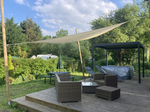 Terrazza esterna con mobili in vimini, tenda parasole e jacuzzi al Luxe Lodge, Flower Camping de la Trye, Francia.