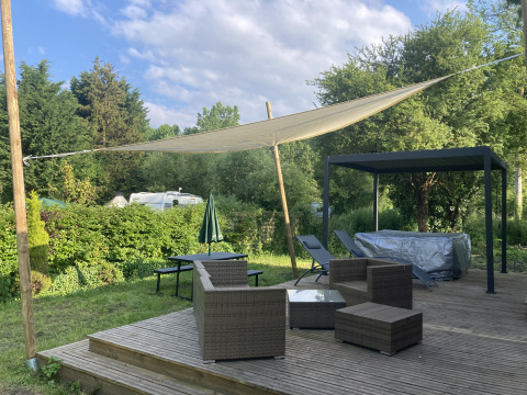 Buitenterras met vlechtwerkmeubels, schaduwzeil en jacuzzi bij Luxe Lodge, Flower Camping de la Trye, Frankrijk.