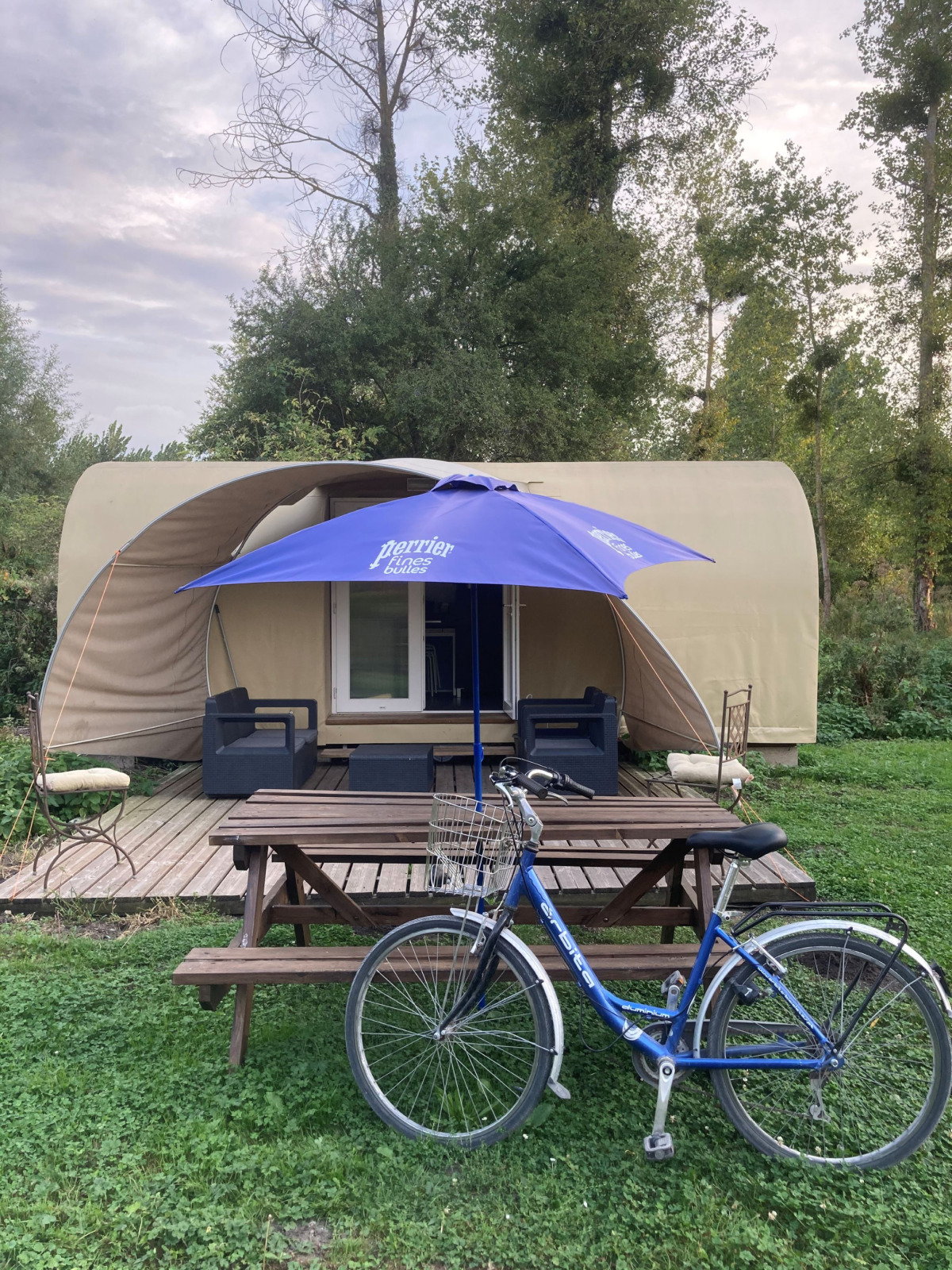 Safaritent Cocosweet bij Flower Camping de la Trye in Frankrijk met fiets, picknickbank en blauwe parasol.