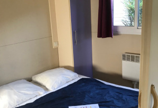 Bedroom in the Green Chalet at Flower Camping de la Trye in France, featuring a bed, wardrobe and window.