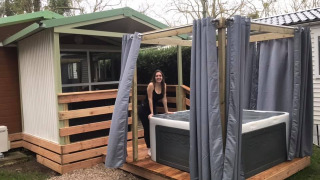 Vrouw aan een buitenjacuzzi met gordijnen bij Chalet du Bélier. Houten terras en groene omgeving.