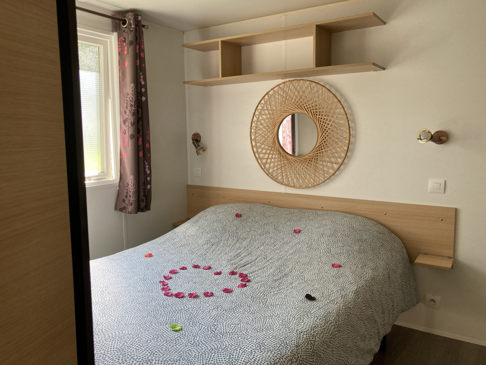 Sfeervolle glamping slaapkamer met tweepersoonsbed, ronde spiegel, plank en rozenblaadjes op het bed.