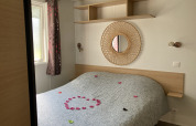 Sfeervolle glamping slaapkamer met tweepersoonsbed, ronde spiegel, plank en rozenblaadjes op het bed.