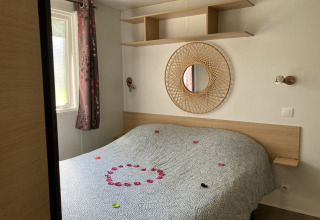 Gezellige glampingkamer met tweepersoonsbed, ronde spiegel, bovenplank en rozenblaadjes op het bed.