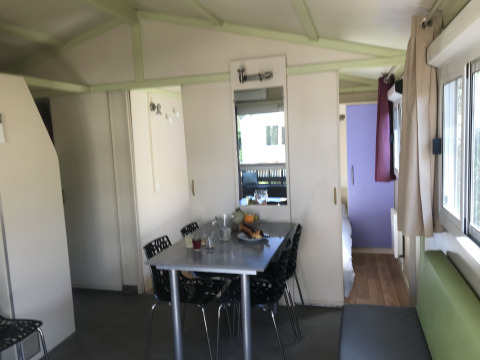 Interieur van Chalet du Bélier + Jacuzzi bij Flower Camping de la Trye, met eettafel en ramen zichtbaar.