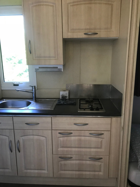 Moderne keuken met lichte houten kasten, gootsteen en gasfornuis in Chalet du Bélier, Flower Camping de la Trye, Frankrijk.