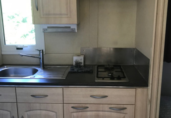 Moderne køkken med lyst træskabe, gaskomfur, vask og vindue, Chalet du Bélier, Flower Camping de la Trye, Frankrig.