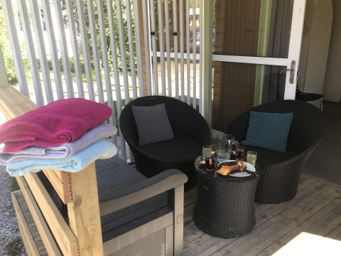 Buitenpatio met rotan stoelen, tafel met drankjes en taart, handdoeken op een houten bank.