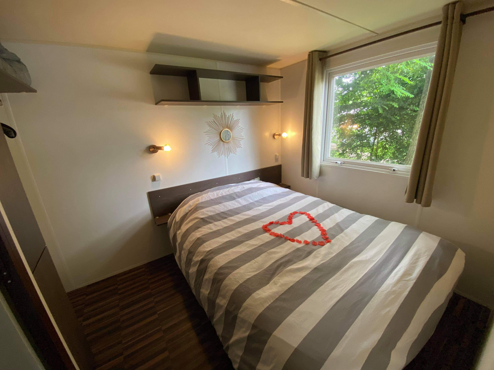 Slaapkamer in Bungalow Les Croisettes met gestreept dekbed en hart van rozenblaadjes bij Flower Camping de la Trye.