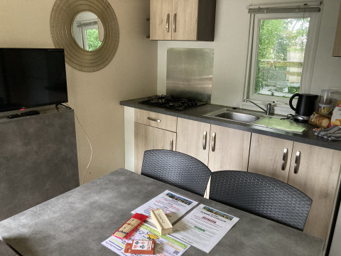 Interieur van Bungalow Les Croisettes met keuken, tafel en brochures bij Flower Camping de la Trye.