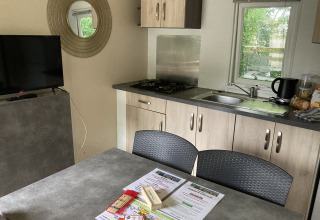 Interieur van Bungalow Les Croisettes met keuken, tafel en brochures bij Flower Camping de la Trye.