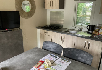 Vista interna del Bungalow Les Croisettes con cucina, tavolo e opuscoli al Flower Camping de la Trye.