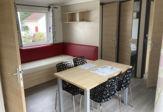 Interni della Mobile home «Grand Confort» al Flower Camping de la Trye, Francia, con tavolo e divano ad angolo.