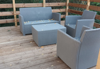 Terraza de madera exterior con muebles de mimbre gris en Mobile home 'Grand Confort', Flower Camping de la Trye.