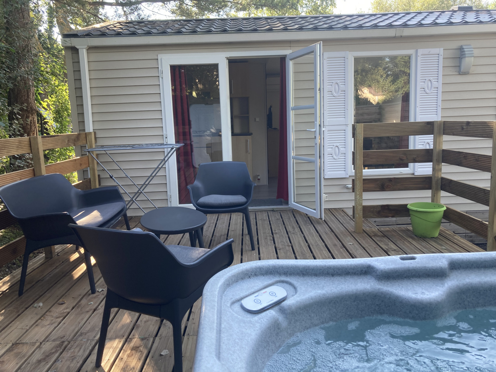 Houten terras met zwarte stoelen, tafel, jacuzzi en bungalow bij Flower Camping de la Trye in Frankrijk.