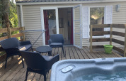 Houten terras met zwarte stoelen, tafel, jacuzzi en bungalow bij Flower Camping de la Trye in Frankrijk.