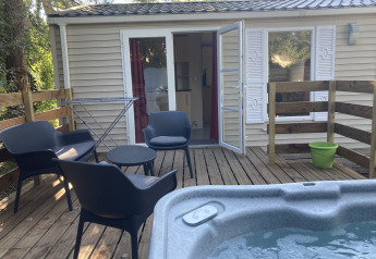 Wooden deck with black chairs, round table, jacuzzi and bungalow at Flower Camping de la Trye in France.
