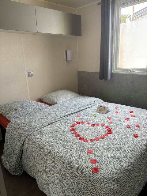 Gezellige lodge slaapkamer met rozenblaadjes in hartvorm en een kaartje op het bed naast het raam.