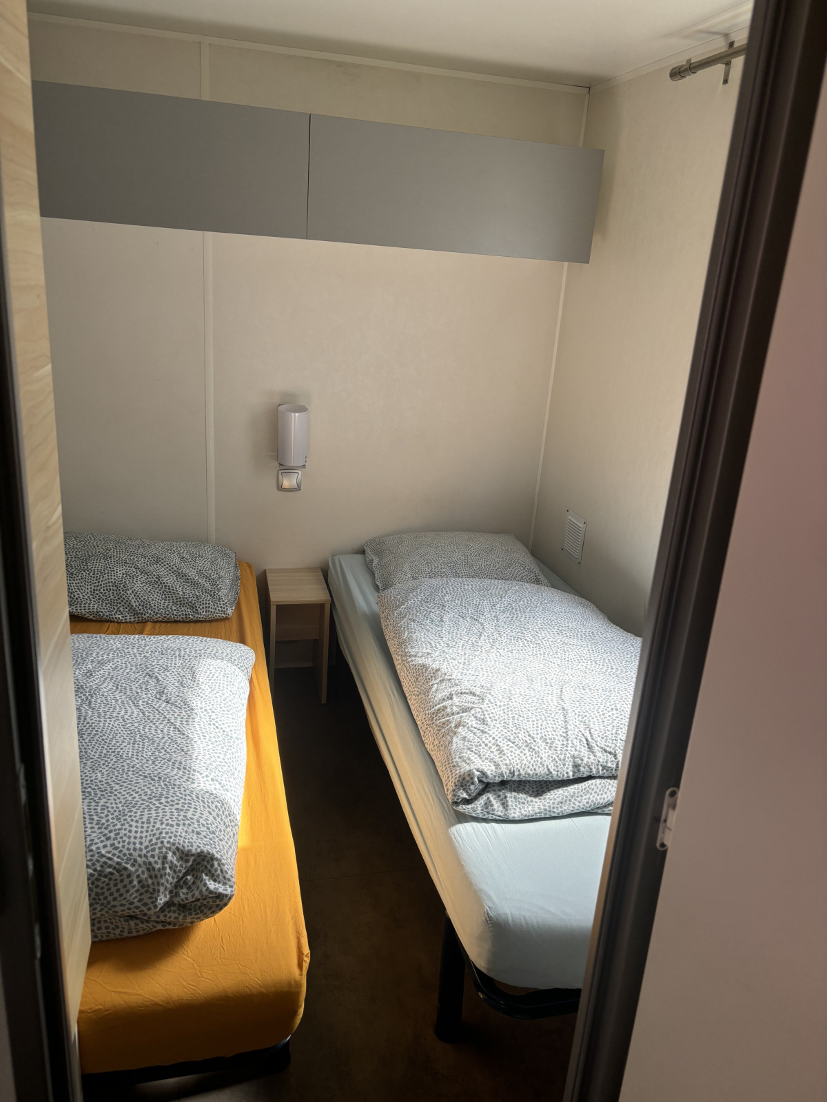 Kleine kamer met twee eenpersoonsbedden en een nachtkastje in Bungalow La Folle Entreprise bij Flower Camping de la Trye.