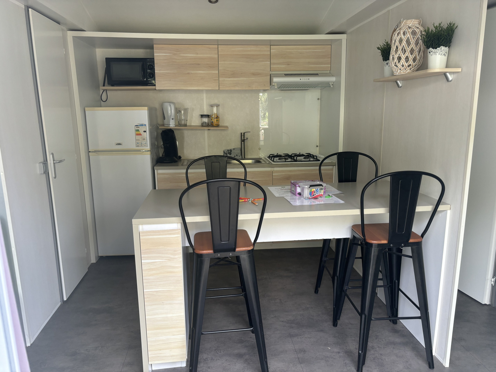Compacte lodge-keuken met eettafel, vier hoge stoelen en moderne apparatuur, inclusief gasfornuis.