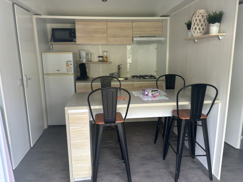 Compacte lodge-keuken met eettafel, vier hoge stoelen en hedendaagse toestellen, inclusief gasfornuis.