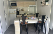 Compacte lodge-keuken met eettafel, vier hoge stoelen en moderne apparatuur, inclusief gasfornuis.