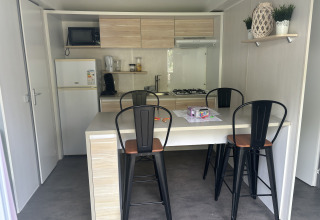 Compacte lodge-keuken met eettafel, vier hoge stoelen en hedendaagse toestellen, inclusief gasfornuis.