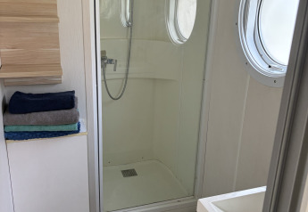 A modern lodge bathroom with a glass shower, round porthole windows, folded towels, and a sink