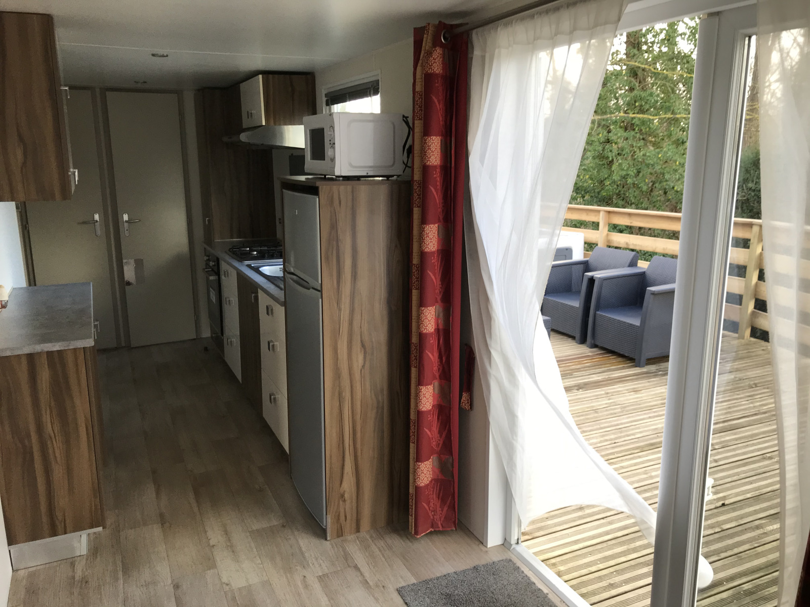 Modern lodge-interieur met keuken, open deuren en houten terras met zitgedeelte op Franse camping.