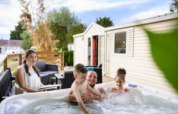 Gezin ontspant in jacuzzi bij hun lodge, Bungalow du Gorguet, op Flower Camping de la Trye in Frankrijk.