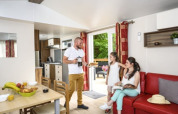 Gezin samen in de woonkamer van Bungalow du Gorguet met keuken, rode bank en uitzicht op het terras in Frankrijk.