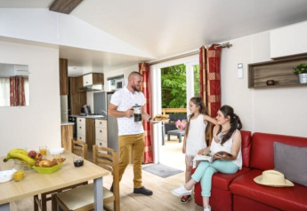 Family relaxing in the living area of Bungalow du Gorguet with kitchen, red sofa, and terrace view in France.