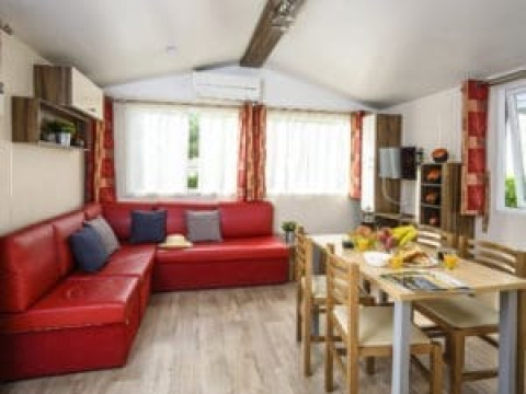 Binnenzicht van Bungalow du Gorguet met rode zetel, eettafel en ramen bij Flower Camping de la Trye in Frankrijk.
