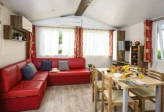 Binnenzicht van Bungalow du Gorguet met rode zetel, eettafel en ramen bij Flower Camping de la Trye in Frankrijk.