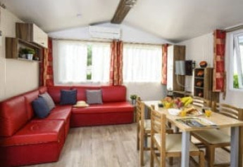 Interior of Bungalow du Gorguet with red couch, dining table, and windows at Flower Camping de la Trye, France.