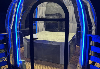 Transparante koepel met bubbelbad, verlicht door blauwe LED-verlichting bij nachtelijk glampingverblijf.