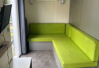 Woonkamer in Bungalow Le Grand Marais met groene zetel en airco, Flower Camping de la Trye, Frankrijk.