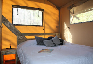 Interieur van Safari Lodge tent op Camping Moulin de Chaules in Frankrijk, zichtbaar bed en ramen.