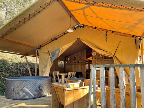 Safari Lodge tent at Campsite Moulin de Chaules in France, showing a wooden deck, seating, and hot tub.