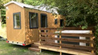 Photo d'une Tiny House + jacuzzi, petite cabane en bois avec terrasse, entourée d'arbres verdoyants.