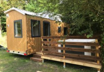 Photo d'une Tiny House + jacuzzi, petite cabane en bois avec terrasse, entourée d'arbres verdoyants.