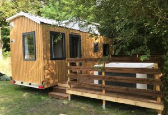 Foto van een tiny house genaamd Tiny House + jacuzzi met houten terras, omgeven door groene bomen.