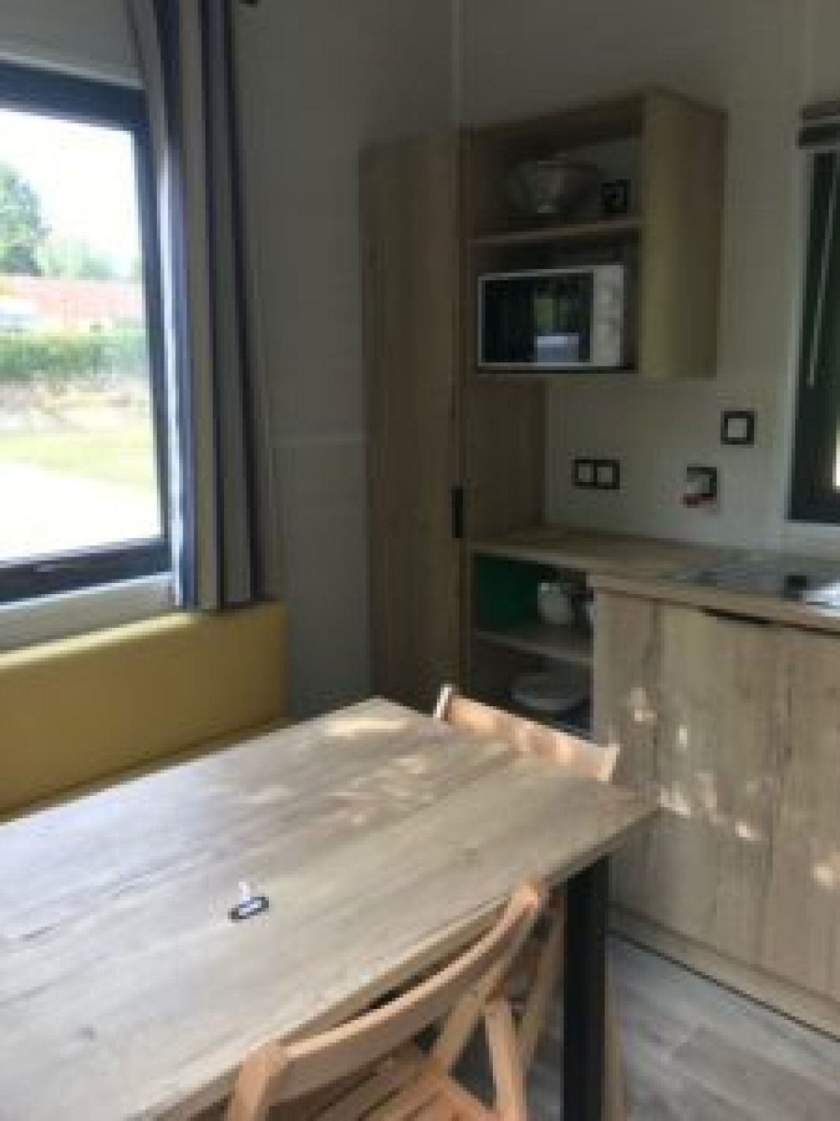 Interieur van een tiny house met eettafel, stoelen en kitchenette bij Flower Camping de la Trye.